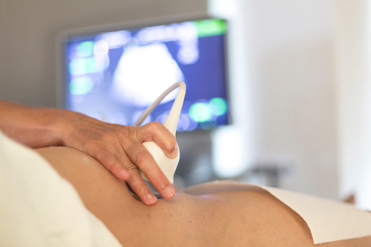 „Hand mit Sonde scannt schwangeren Bauch, Ultraschallbild von Fötus auf Monitor.“